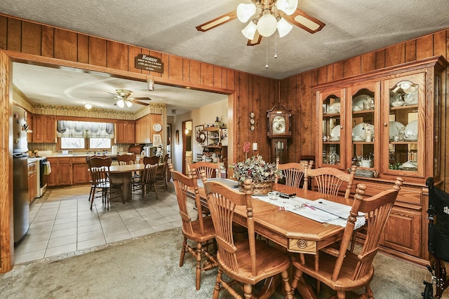 dining space with light tile patterned floors, wooden walls, a ceiling fan, and a textured ceiling