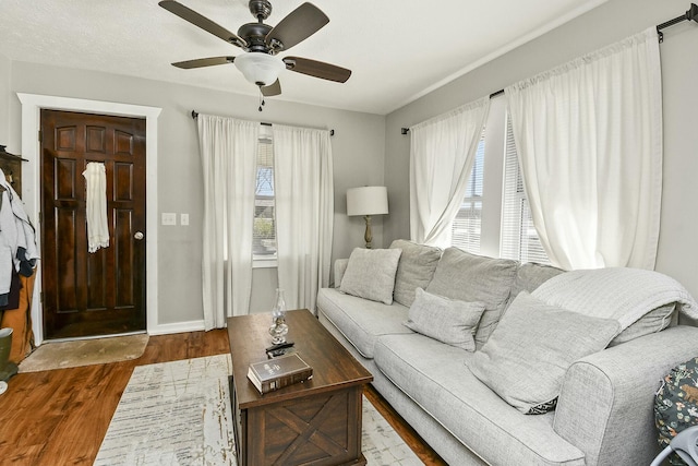 living area with wood finished floors, a ceiling fan, and baseboards