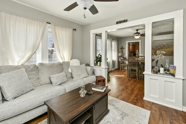 living area featuring dark wood-style floors, a wall unit AC, and a ceiling fan