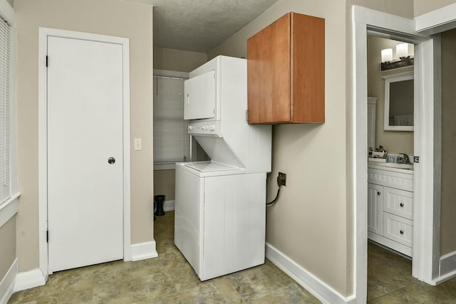 laundry area with a textured ceiling, stacked washer / dryer, cabinet space, and baseboards