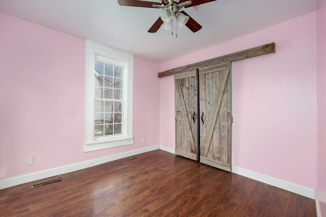 unfurnished bedroom featuring visible vents, a barn door, ceiling fan, wood finished floors, and baseboards