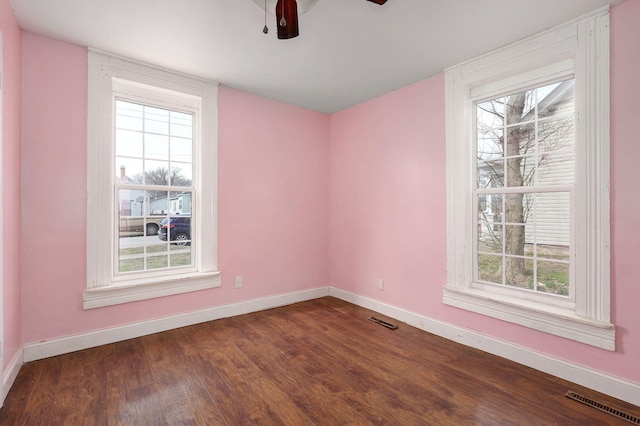 spare room with baseboards, visible vents, dark wood finished floors, and a ceiling fan