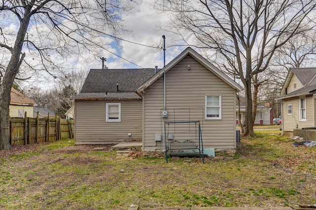 rear view of house with a shingled roof and fence