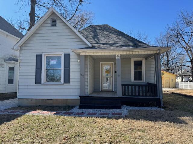 bungalow-style home featuring covered porch, a front yard, and roof with shingles