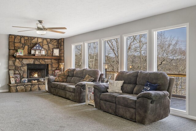 carpeted living room featuring a healthy amount of sunlight, ceiling fan, a stone fireplace, and a textured ceiling