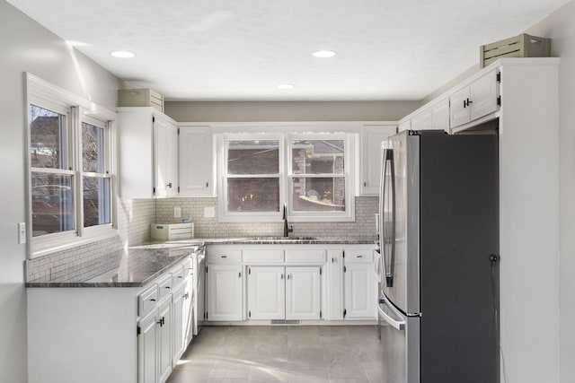 kitchen featuring white cabinetry, dark stone counters, a sink, and freestanding refrigerator