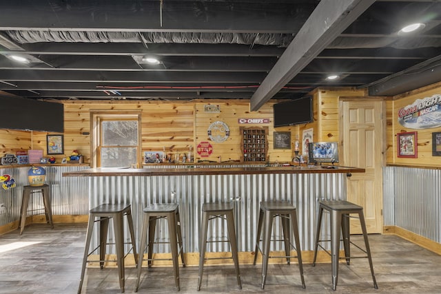 bar with beam ceiling, a dry bar, wood walls, wood finished floors, and baseboards