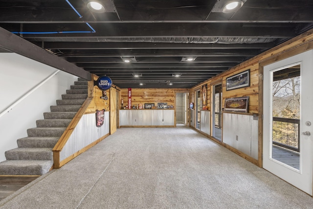 below grade area featuring carpet, wooden walls, and stairs