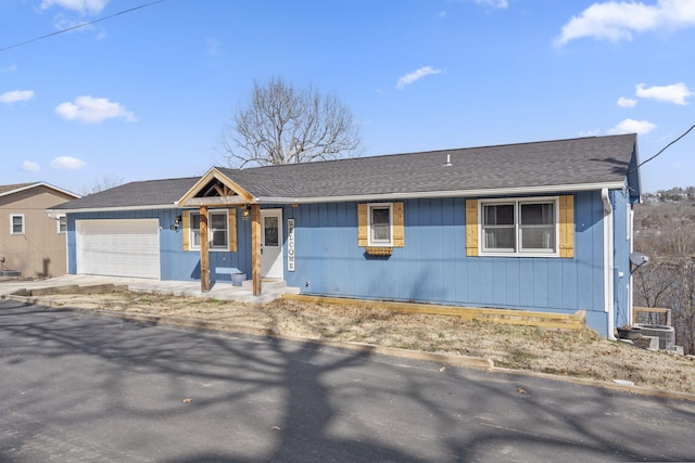 ranch-style house featuring driveway, central AC unit, roof with shingles, and an attached garage