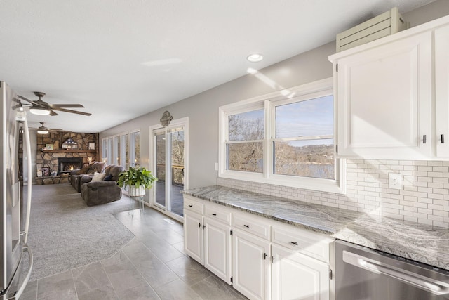 kitchen with stainless steel appliances, a fireplace, open floor plan, light stone countertops, and tasteful backsplash