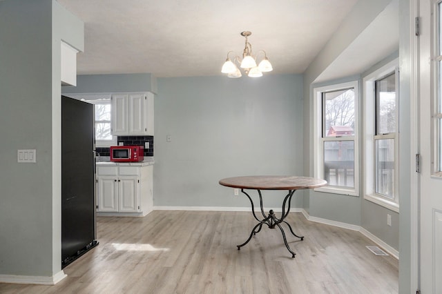 dining space featuring a notable chandelier, light wood-style flooring, visible vents, and baseboards