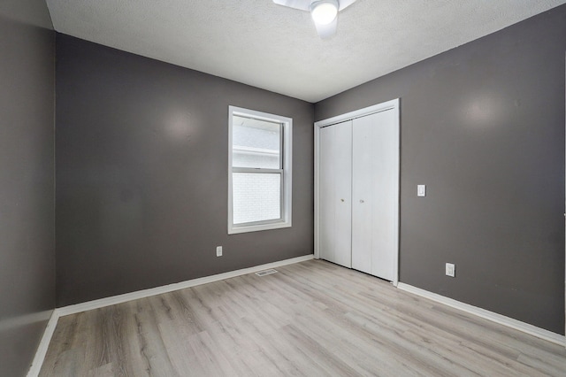 unfurnished bedroom featuring a textured ceiling, visible vents, baseboards, a closet, and light wood finished floors