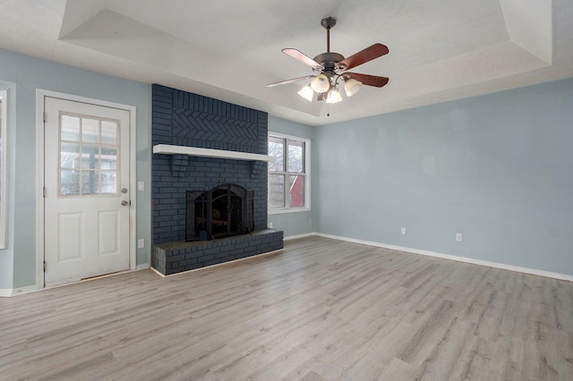 unfurnished living room with wood finished floors, a fireplace, a raised ceiling, and baseboards