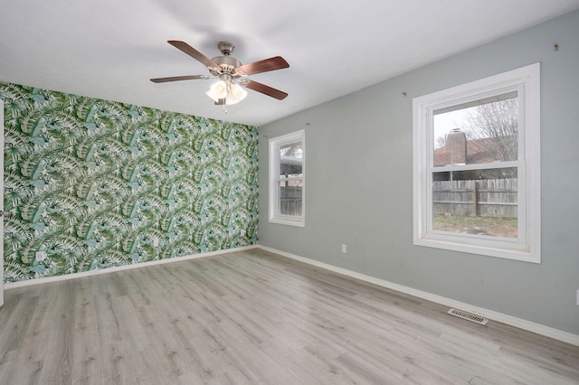 empty room with wood finished floors, visible vents, baseboards, and wallpapered walls