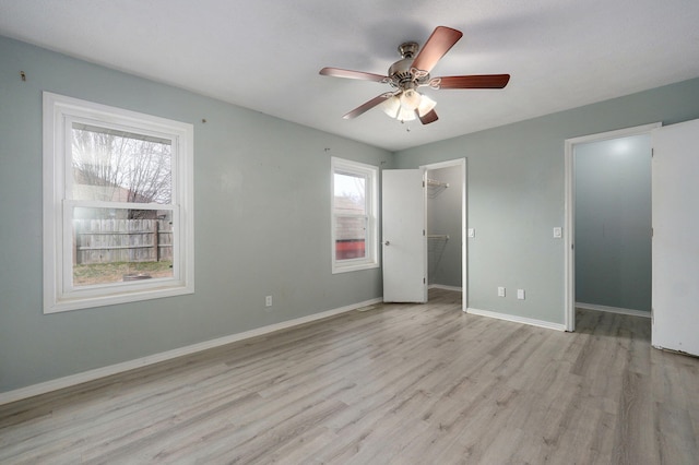 unfurnished bedroom featuring a closet, a spacious closet, baseboards, and wood finished floors