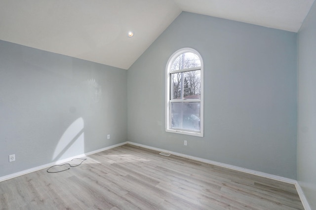 spare room with light wood-type flooring, visible vents, vaulted ceiling, and baseboards