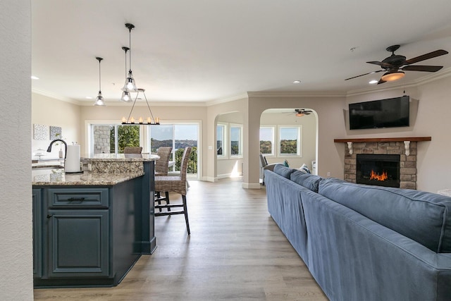 living room featuring a fireplace, recessed lighting, ornamental molding, light wood-type flooring, and baseboards