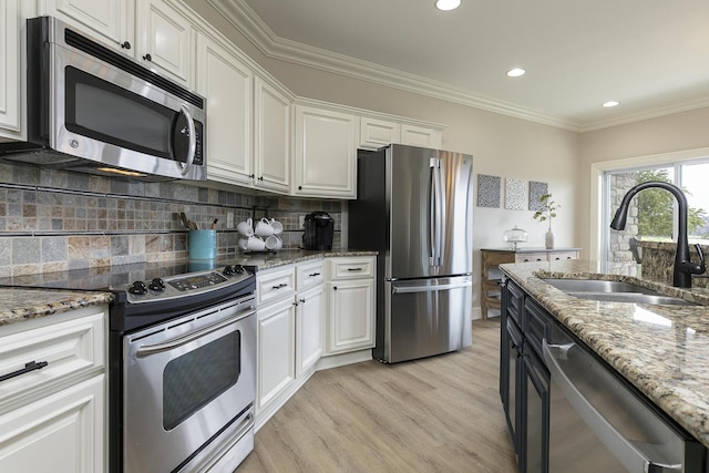 kitchen with crown molding, stainless steel appliances, light wood-style floors, white cabinetry, and a sink