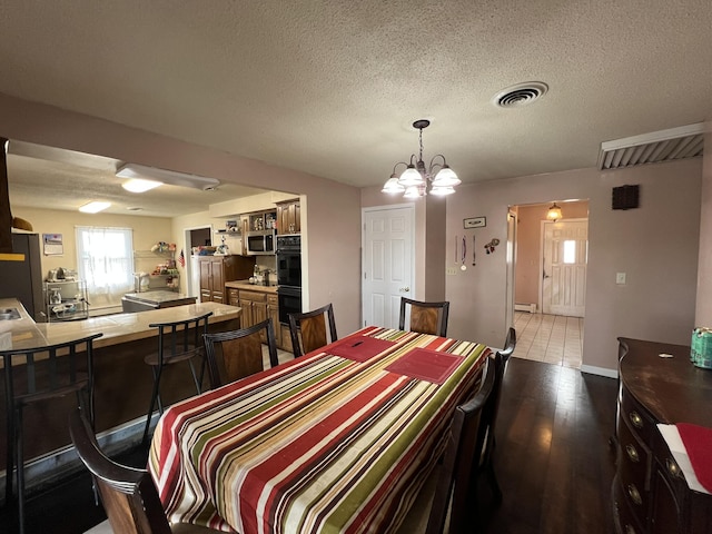 dining space featuring visible vents, light wood-style flooring, baseboard heating, an inviting chandelier, and a textured ceiling