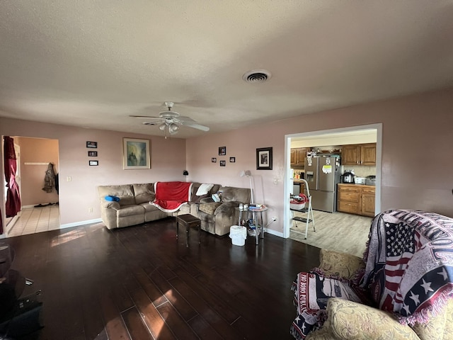 living room with visible vents, light wood-style flooring, a ceiling fan, a textured ceiling, and baseboards