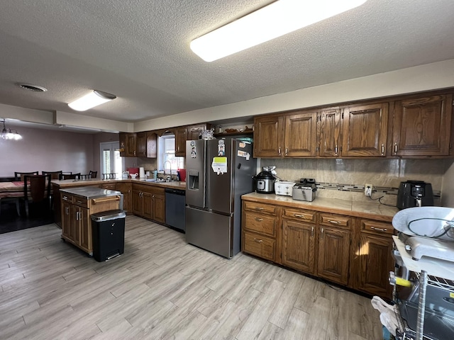 kitchen featuring light wood finished floors, tasteful backsplash, stainless steel fridge with ice dispenser, dishwashing machine, and a sink