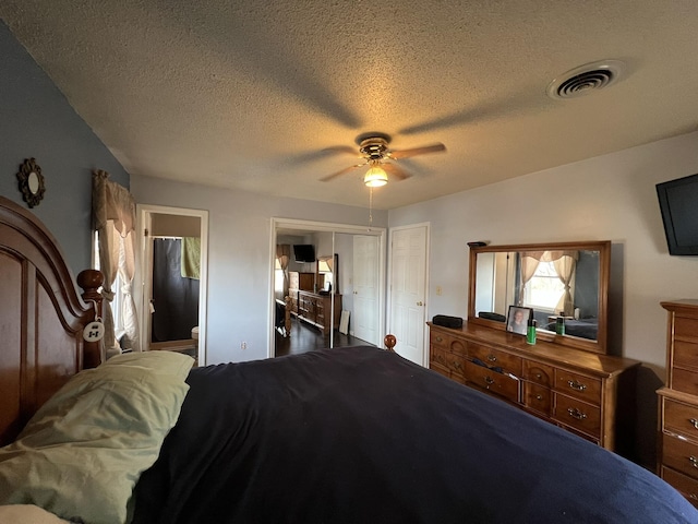 bedroom featuring a ceiling fan, ensuite bath, visible vents, and a textured ceiling