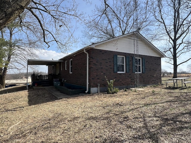 view of side of home featuring dirt driveway, an attached carport, and brick siding