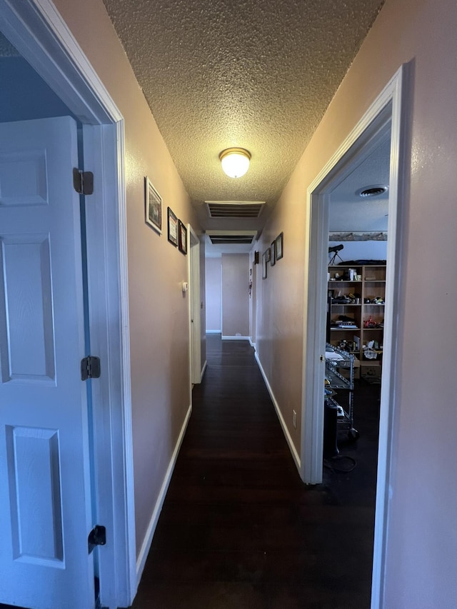 hallway featuring visible vents, a textured ceiling, baseboards, and wood finished floors