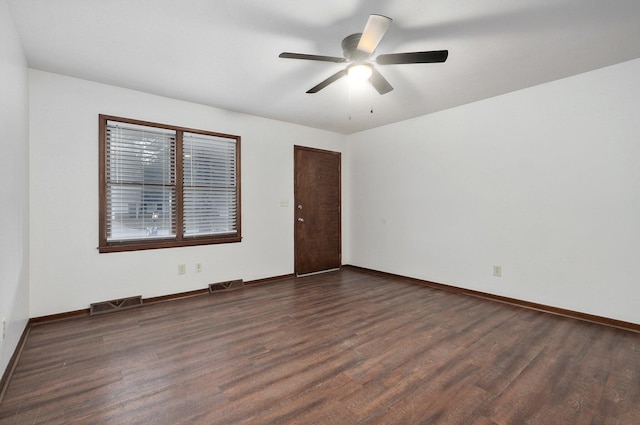 empty room with dark wood-type flooring, a ceiling fan, visible vents, and baseboards