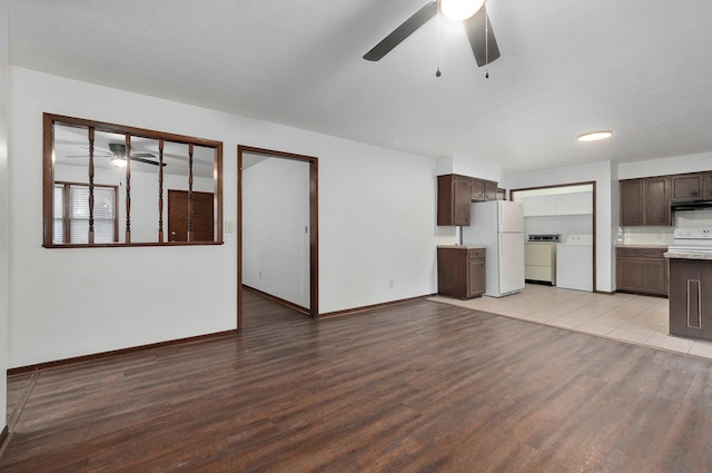 unfurnished living room with a ceiling fan, baseboards, light wood finished floors, and separate washer and dryer