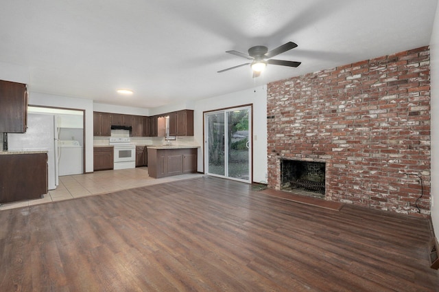 unfurnished living room featuring light wood finished floors, washer / dryer, ceiling fan, a fireplace, and a sink