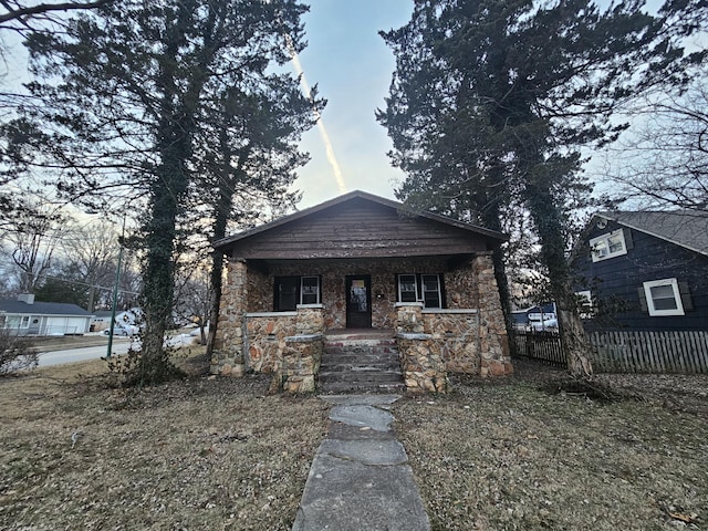 bungalow-style home featuring stone siding, a porch, and fence