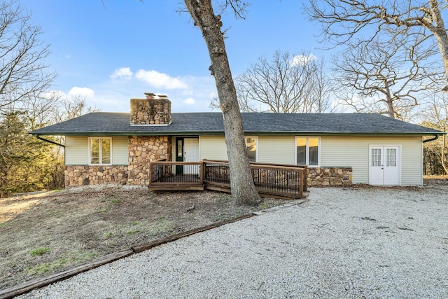 view of front of house with a deck, stone siding, a shingled roof, and a chimney