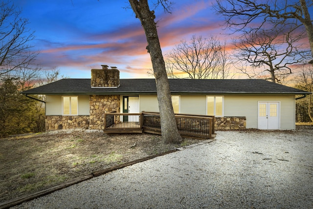 view of front of home featuring gravel driveway, stone siding, a chimney, and a wooden deck