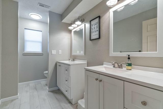 bathroom with two vanities, visible vents, toilet, a sink, and a textured ceiling