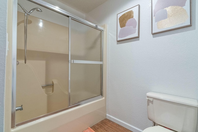 full bathroom featuring a textured wall, toilet, bath / shower combo with glass door, wood finished floors, and baseboards