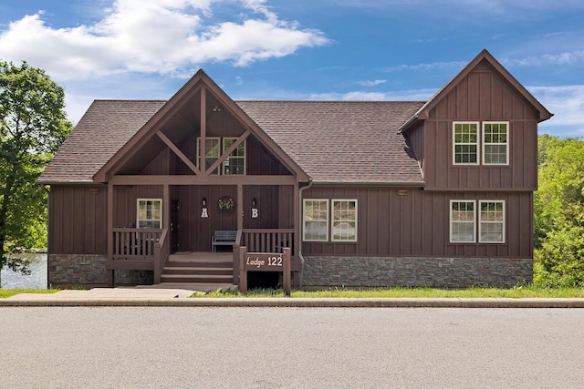 rustic home with covered porch, a shingled roof, stone siding, and board and batten siding