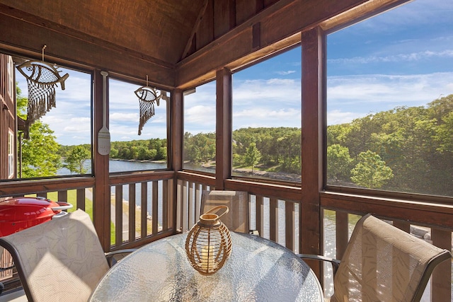 sunroom / solarium with lofted ceiling, a water view, plenty of natural light, and a wooded view