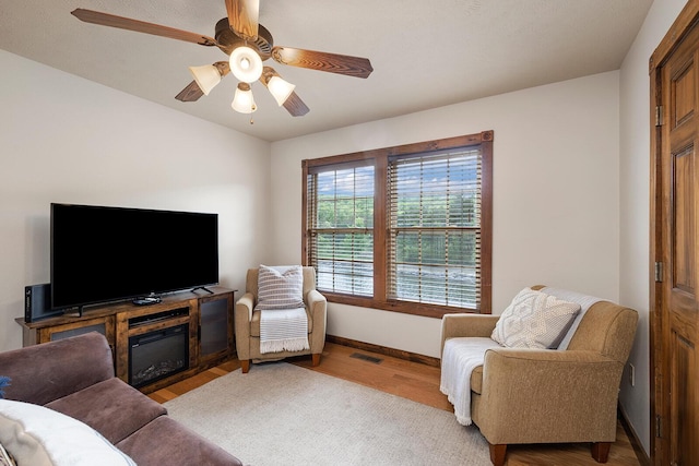 living room with a ceiling fan, visible vents, baseboards, and wood finished floors