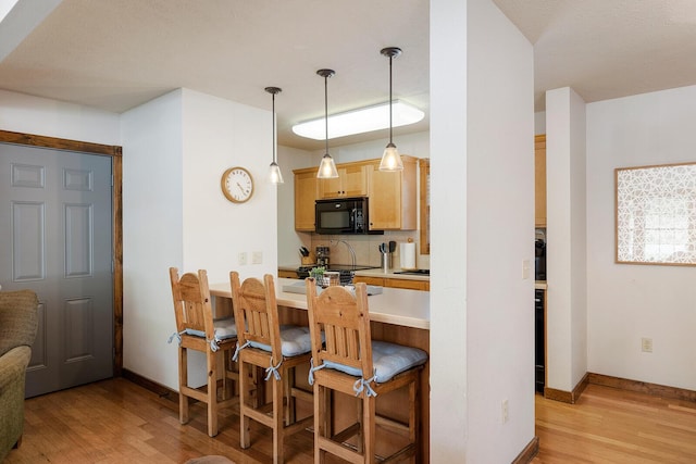 kitchen featuring black microwave, light wood-style flooring, a kitchen breakfast bar, and backsplash