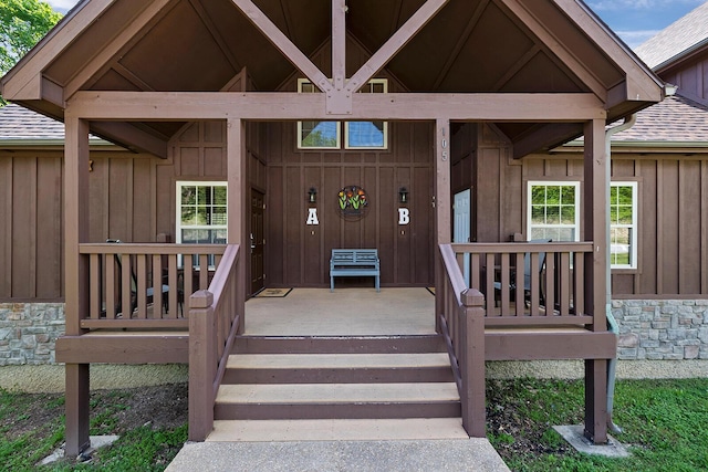 view of exterior entry with board and batten siding, stone siding, a shingled roof, and a porch