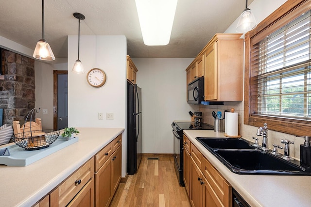 kitchen featuring light countertops, hanging light fixtures, light wood-style floors, a sink, and black appliances