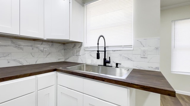 kitchen with white cabinets, wood counters, ornamental molding, a sink, and backsplash