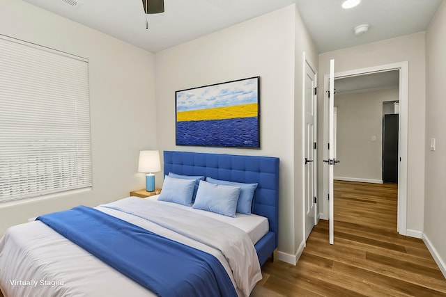 bedroom with a ceiling fan, visible vents, baseboards, and wood finished floors