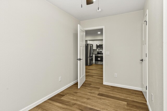 unfurnished bedroom featuring a ceiling fan, wood finished floors, freestanding refrigerator, and baseboards