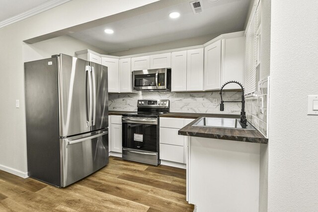 kitchen with stainless steel appliances, a sink, visible vents, white cabinets, and dark countertops