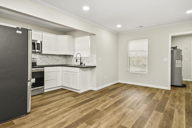 kitchen featuring stainless steel appliances, a sink, water heater, dark countertops, and crown molding