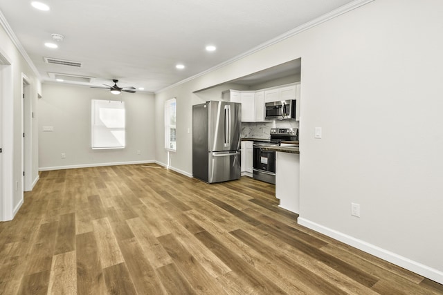 kitchen featuring stainless steel appliances, white cabinetry, tasteful backsplash, dark countertops, and crown molding