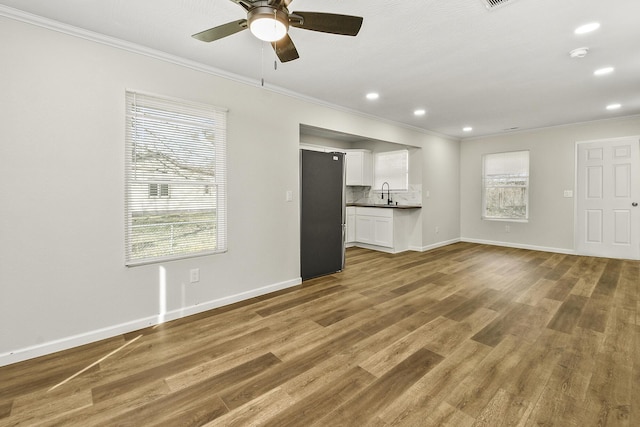 unfurnished living room featuring a sink, ornamental molding, wood finished floors, and baseboards