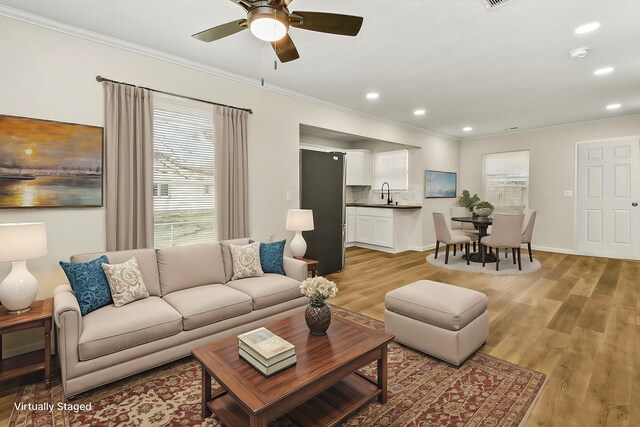 living area with light wood-style floors, recessed lighting, ornamental molding, and baseboards